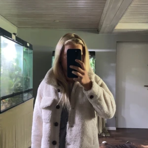 Vit teddyjacka från Lindex - Säljer en supermysig vit teddyjacka från Lindex i storlek 134/140. Jackan har en skön och fluffig textur som håller dig varm under kalla dagar. Den har långa ärmar och knappar framtill, samt två stora fickor på bröstet. Perfekt för höst och vinter! 🧥❄️