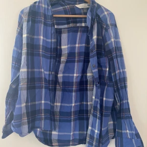 Blå och vit rutig skjorta - Säljer en snygg blå och vit rutig skjorta. Den har långa ärmar och knappar framtill. Perfekt för en avslappnad stil eller som en overshirt. Skjortan är i bra skick och passar till vardags. Tillverkad i Indien.  