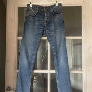 Säljer ett par snygga blå jeans från Nudie Jeans i modellen Grim Tim. De är i storlek W30 L32 och är tillverkade av 98% ekologisk bomull och 2% elastan, vilket gör dem både bekväma och stretchiga. Perfekta för vardagsbruk!