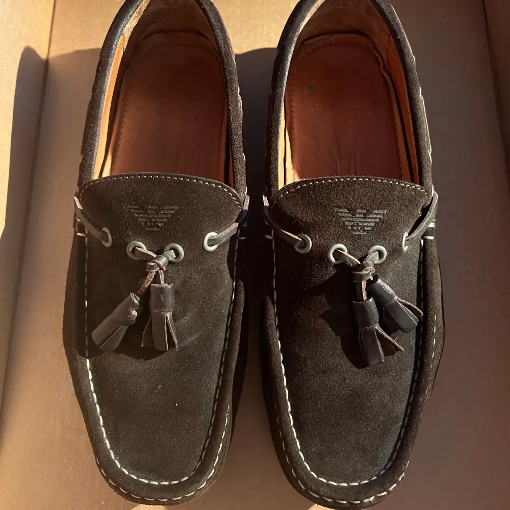 Bruna loafers i mocka från Armani Jeans. Klassisk design med snörning och tofsdetaljer på ovansidan.. Skor.