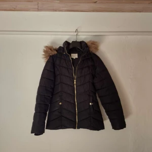 Jacka fårn Kappahl - Jackan är svart med en guld kedja, och päls på luvan. Luvan går att att av och sätta på med hjälp av knappar med ena knappen är sönder, annars är jackan i bra skick. Säljs för att den blivit liten 
