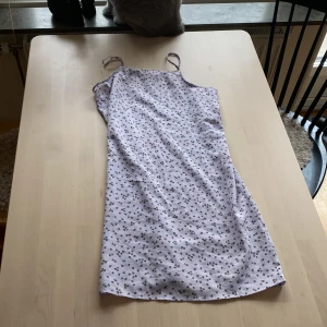 Ljuslila blommig klänning från H&M - Säljer en söt ljuslila klänning från H&M med små bruna blommor. Klänningen är ärmlös och har smala axelband. Perfekt för sommaren eller en festlig tillställning. Den är i bra skick och redo för en ny ägare!