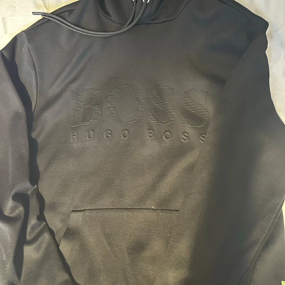 Säljer en snygg och stilren svart hoodie från Hugo Boss. Den har en stor BOSS-logga på framsidan och en praktisk magficka. Hoodien är perfekt för både vardag och chill. Den är i bra skick och superbekväm att ha på sig. Passar perfekt till höst och vinter!. Tröjor & Koftor.