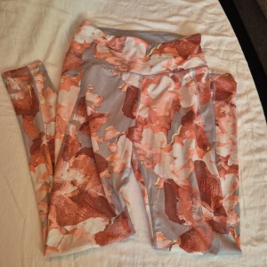 Mönstrade leggings från H&M Sport - Säljer ett par snygga och bekväma leggings från H&M Sport. De är i storlek S och har ett coolt mönster i rosa och vitt på en ljusgrå bakgrund. Perfekta för träning eller en avslappnad dag. De är i bra skick och redo för en ny ägare!