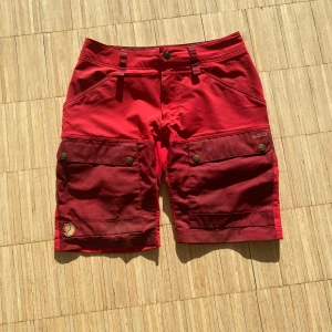 Röda shorts från Fjällräven - Säljer ett par röda shorts från Fjällräven i storlek S.  Den har några små fläckar som förmodligen går bort i tvätten men är väldigt bra skick för använda friluftsbyxor.