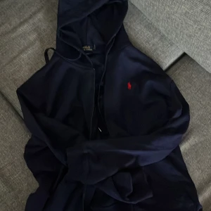 Ralph Lauren zipper - Säljer en Ralph Lauren zipper i marinblå med rött emblem. Buren ett fåtal gånger, säljer för den ej kommer till användning längre. Skriv vid minsta fråga. Storlek L