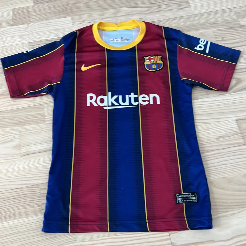 Säljer en Barcelona fotbollströja från Nike i nyskick. Tröjan är röd och blå med gula detaljer. Den är tillverkad i Dri-Fit material som håller dig sval och torr under matchen. Perfekt för alla Barca-fans! Du får med shortsen. T-shirts.