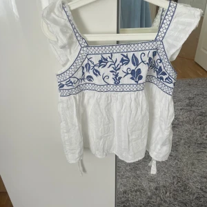 Vit/blå blus - Vit blus med blå broderi på framsidan och på ärmarna.