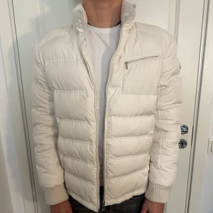 Vit Stilren Dunjacka från Sergio Tachini - Säljer en snygg vit dunjacka från Sergio Tacchini. Jackan har en dragkedja framtill och en bröstficka med dragkedja. Den är quiltad och har en hög krage som håller dig varm. Perfekt för vintern! Jackan är i nyskick! Storlek L men passar som M och även S. Modellen är 182 cm och väger 75 kg. Pris går att diskuteras!
