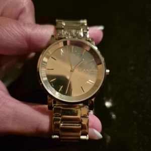 Guldfärgad klocka från DKNY - Elegant guldfärgad klocka från DKNY med en stilren urtavla och metallarmband. Perfekt för att ge en lyxig touch till din outfit.