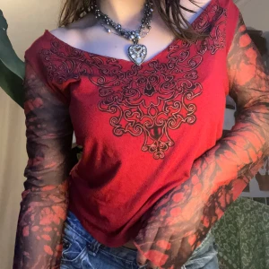 Röd topp med mönstrade ärmar - Snygg röd topp med unikt svart mönster framtill och transparenta, mönstrade mesh ärmar. Perfekt för en trendig look. 