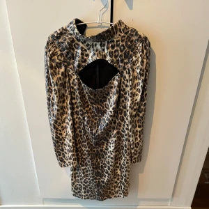 Leopardmönstrad klänning från No Man's Label - Snygg leopardmönstrad klänning från No Man's Label med glittriga paljetter och en öppen rygg. Klänningen har långa ärmar och är tillverkad i 100% polyester.