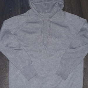 Grå merino hoodie - Mysig grå hoodie med justerbar huva och långa ärmar. Perfekt för kyliga dagar och avslappnade stunder. Ribbstickade muddar vid ärmslut och nederkant för extra komfort.