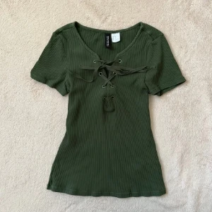 Olivgrön ribbad topp med snörning - Snygg olivgrön ribbad topp från H&M med korta ärmar och snörning framtill. Gott skick strl XS.