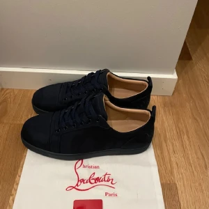 Marinblå sneakers från Christian Louboutin - Ej användt ! Snygga marinblå sneakers i mocka från Christian Louboutin med den ikoniska röda sulan. Skorna har snörning och en stilren design som passar perfekt för en trendig look.