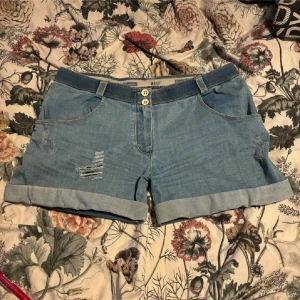 Blå jeansshorts från Freddy - Snygga blå jeansshorts från Freddy med slitna detaljer och uppvikta ben. De har två knappar framtill och klassiska femficksdesign. Perfekta för en avslappnad sommarlook!