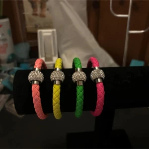 Färgglada flätade armband med strassdetaljer - Säljer ett set med fyra färgglada flätade armband i rosa, gul, grön och cerise. Varje armband har en glittrig strassdetalj i silverfärg. Perfekt för att lägga till en färgklick till din outfit!