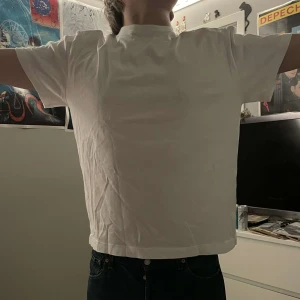 Vit t-shirt med smiley från Weekday - Säljer en vit t-shirt från Weekday med en stor svart smiley på baksidan. T-shirten har korta ärmar och en klassisk passform. Perfekt för en avslappnad stil.