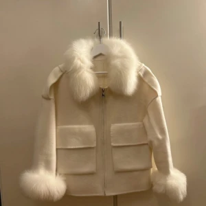 Vit jacka med pälsdetaljer - Säljer en stilren vit jacka med fluffiga pälsdetaljer på krage och ärmslut. Jackan har en dragkedja framtill och två stora fickor. Perfekt för kyliga dagar när du vill hålla dig varm och snygg. Nypris 3800. Använd en gång. 