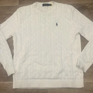 Vit stickad tröja från Ralph Lauren - Säljer en stilren vit stickad tröja från Ralph Lauren med det klassiska logotypbroderiet på bröstet. Tröjan har en rund halsringning och långa ärmar, perfekt för kyligare dagar. Passar både till jeans och chinos för en avslappnad look.