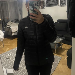 Svart dunjacka från Adidas / kurtka puchowa  - En tunn svart höst/vår jacka från Adidas i storlek M, köpt ifrån stadium. Väldigt skön och lätt den är inte stel heller perfekt för dig med lite längre armar ( köparen står för frakt! )