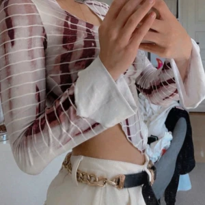 Randig transparent topp - Snygg och trendig transparent topp med randigt mönster i vitt och vinrött. Toppen är croppad och har långa ärmar med en lätt utsvängd design. Perfekt för en stilren och modern look.