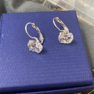 Silverfärgade örhängen med stora stenar - Eleganta silverfärgade örhängen med stora, gnistrande stenar. Perfekta för att ge en touch av glamour till din look. De har en enkel och stilren design som passar till många tillfällen.