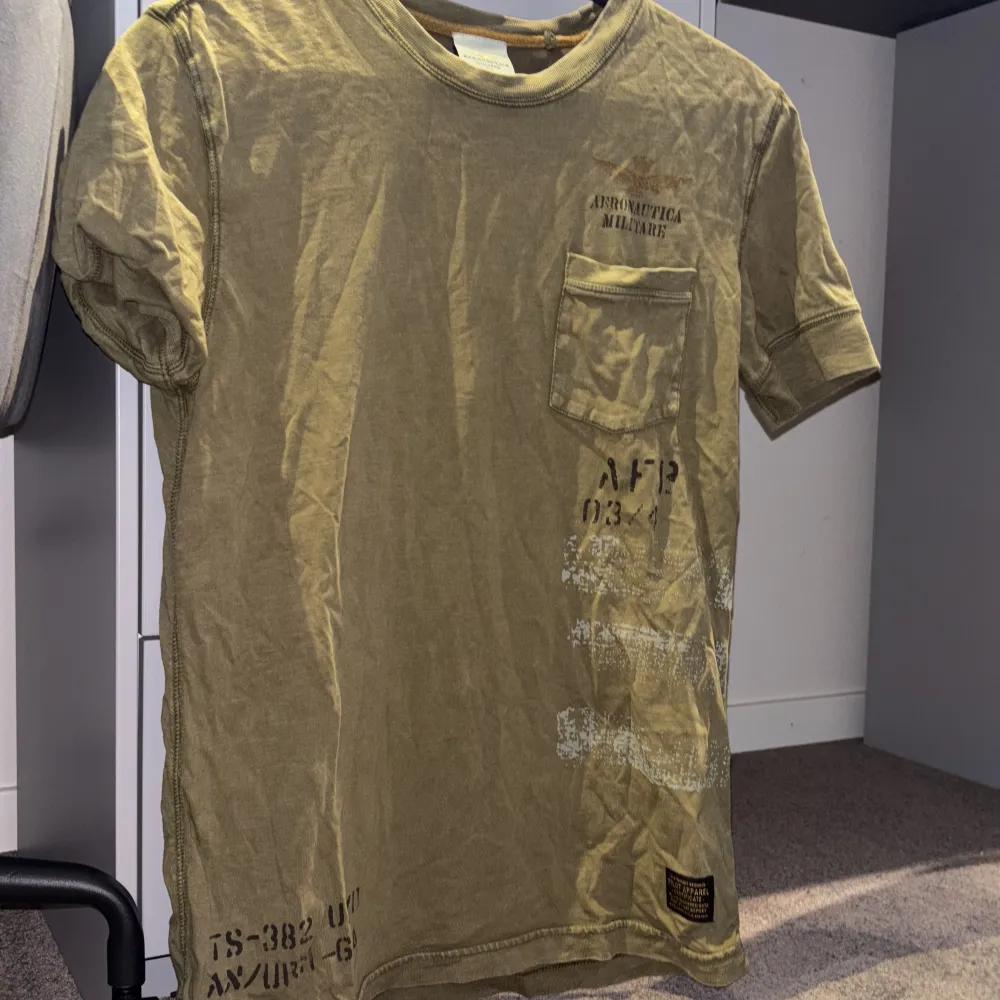 Snygg olivgrön t-shirt från Aeronautica Militare med tryck på bröstet och en praktisk bröstficka. . T-paidat.