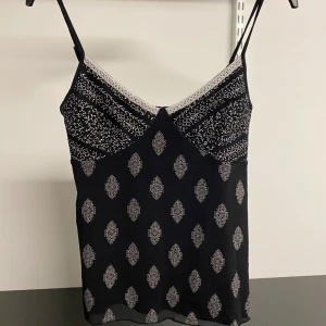 Svart linne med mönster - Snyggt svart linne med vita mönster och spetsdetaljer vid halsen. Perfekt för en cool look