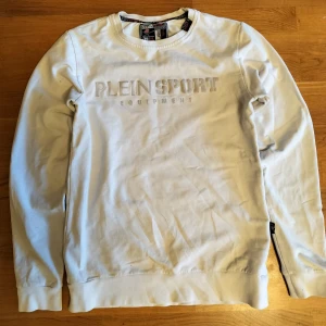 Vit sweatshirt från Plein Sport - Säljer en stilren vit sweatshirt från Plein Sport med tryck på både fram- och baksidan. Tröjan har långa ärmar och en rund halsringning. Perfekt för en avslappnad look. Nypris ca 2200kr