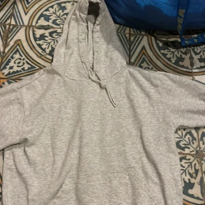 Grå hoodie - Säljer en bekväm grå hoodie med justerbar dragsko i huvan och en praktisk magficka. Perfekt för en avslappnad stil.
