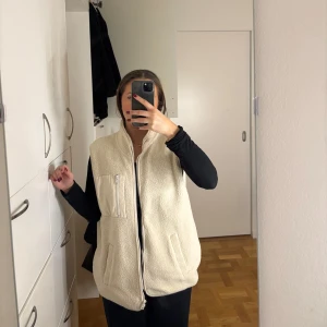 Beige fleeceväst  - Säljer en mysig beige/cremefärgade fleeceväst i teddy material med dragkedja framtill. Västen har en hög krage och praktiska fickor på sidorna. Perfekt för kyliga dagar men även snygg till vardagliga outfits!