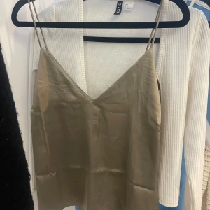 Beige satinlinne från Lager 157 - Snyggt beige linne i satin från Lager 157 med smala axelband och v-ringad design. Perfekt för en stilren och elegant look.