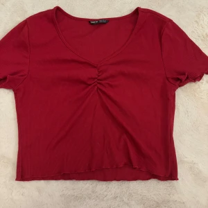 Röd ribbad topp - Snygg röd ribbad topp med v-ringning och rynkdetalj framtill. Kortärmad och croppad design som passar perfekt för en trendig look. Aldrig använd 