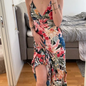 Blommig klänning - Säljer en färgglad blommig klänning med smala axelband och v-ringning. Klänningen har ett vackert blommönster i rött, grönt och blått. Perfekt för sommarens festligheter! Går även att justera midjan med knytning🌸🌺