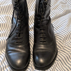 Svarta skinnstövletter med snörning - Snygga svarta stövletter i skinn med snörning och dragkedja på sidan. Perfekta för en stilren eller goth look. De har en spetsig tå och låg klack.