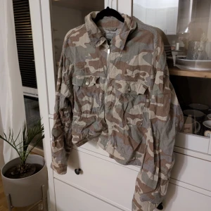 Camouflagejacka från Lindex - Camouflagejacka från Lindex med dragkedja och krage. Jackan har långa ärmar och två bröstfickor med knappar. Storlek M, men passar även en S. 