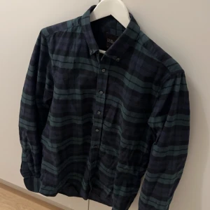 Mörkgrön och svart rutig skjorta - Snygg mörkgrön och svart rutig skjorta med knappar framtill. Perfekt för en avslappnad stil. Skjortan har långa ärmar och en klassisk krage. Sparsamt använd. Nypris hos Oscar Jacobsson i skrivande stund är 1395 kr. 