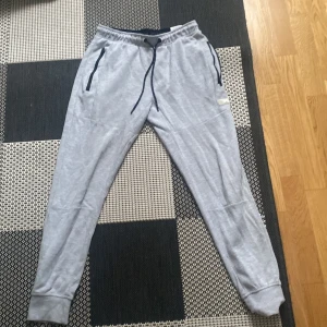 Grå mjukisbyxor från Jack & Jones - Säljer ett par grå mjukisbyxor från Jack & Jones. Byxorna har en elastisk midja med snörning och muddar vid bensluten. Perfekta för en avslappnad stil.