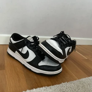 Nike Dunk i svart och vitt - Snygga Nike Dunk sneakers i klassisk svart och vit färgkombination. Skorna har en låg profil med snörning och den ikoniska Nike-loggan på sidan. Perfekta för en stilren look. Har även kvitto om det önskas