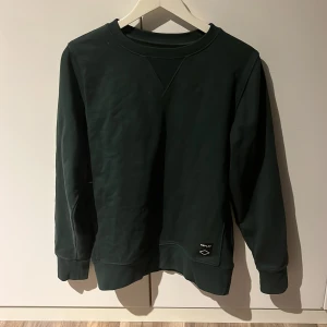 Mörkgrön tröja från Replay - Snygg mörkgrön tröja från Replay med rund hals och långa ärmar. Den är använd en gång. Tröjan har en liten logga på framsidan och ribbade muddar vid ärmslut och nederkant.                                 Storlek: S                                          Nypris: 799kr