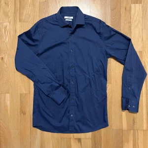 Mörkblå skjorta från Jack & Jones - Snygg mörkblå skjorta från Jack & Jones i slim fit. Använd endast ett fåtal gånger. Skjortan har långa ärmar och knappar framtill. Perfekt för en stilren look. Storlek S passar M