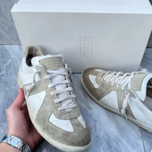 Maison Margiela sneakers i mocka och skinn - Säljer ett par stilrena Maison Margiela sneakers i beige och vit färg. Skorna är gjorda i en kombination av mocka och skinn, vilket ger dem en lyxig känsla. De har klassisk snörning och är i mycket bra skick. Perfekta för både vardag och fest!   storlek 43 så ch Dustbag kommer med. Skriv om frågor och om ni vill köpa. Kom med prisförslag.  Tänker mig runt 3000. De är legit checkade och är såklart äkta!jag kommer inte gå med prisförslag som är helt orimliga!