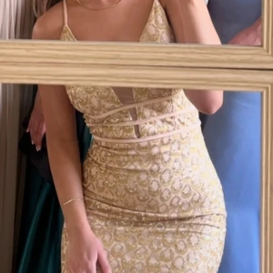 Guldglittrig balklänning - Säljer en fantastisk guldglittrig balklänning med smala axelband och djup v-ringning. Klänningen är tight och perfekt för festliga tillfällen. Den har ett vackert paljettmönster som verkligen fångar ljuset. Perfekt för bal eller någon annan fest❤️