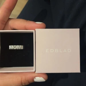 Edblad mom ring  - Säljer en stilren silverring från Edblad med texten 'MOM'. Perfekt present till mamma eller som ett personligt smycke. Ringen kommer i originalförpackning och är i nytt skick. Passar till alla tillfällen och är en fin detalj till vardags eller fest.