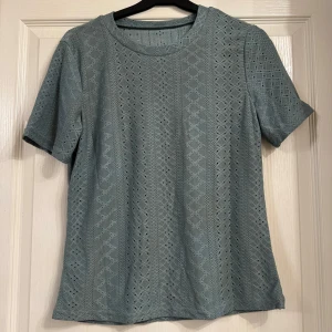 T-shirt Topp storlek S - Den är oanvänd. Säljer en söt blå blus med spetsdetaljer. Den har korta ärmar och ett diskret mönster som ger en elegant touch. Perfekt för både vardag och festliga tillfällen! 