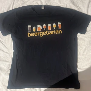 T-shirt beergeetarian tryck - Säljer en svart t-shirt med ett roligt tryck av olika ölglas och texten 'beergeetarian'. Perfekt för ölälskaren! T-shirten är i bra skick. Passar perfekt till avslappnade tillfällen eller en utekväll med vänner.