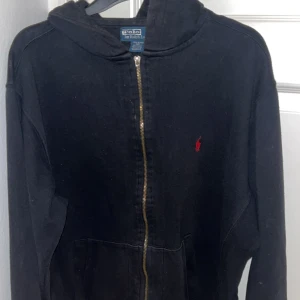 Svart hoodie från Polo Ralph Lauren - Säljer en svart hoodie från Polo Ralph Lauren i bra skick. Den har en dragkedja framtill och en liten röd logga på bröstet. Perfekt för höst och vår, med långa ärmar och en skön passform. Passar både till vardags och chillkvällar.