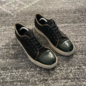 Säljer ett par snygga svarta sneakers från Lanvin i bra skick. De har en glansig tå och snörning, vilket ger dem en stilren look. Perfekta för både vardag och fest! Sulorna är vita med lite slitage, men fortfarande i bra form.