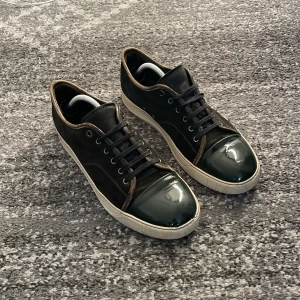 Svarta sneakers från Lanvin - Säljer ett par snygga svarta sneakers från Lanvin i bra skick. De har en glansig tå och snörning, vilket ger dem en stilren look. Perfekta för både vardag och fest! Sulorna är vita med lite slitage, men fortfarande i bra form.